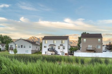 Evleri ve dağları olan yeşil çimlerle çevrili gölet bulutlu mavi gökyüzüne karşı