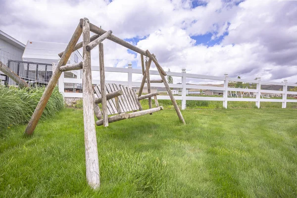 Vecchio giardino in legno altalena su erba verde lussureggiante all'interno recinzione picchetto bianco — Foto Stock