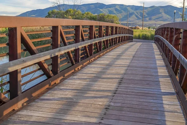 山の景色を望む湖の上の橋の日当たりの良い木製のデッキと手すり — ストック写真