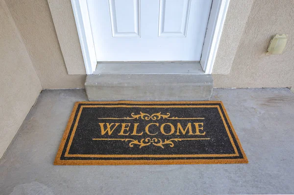 Black and brown Welcome doormat by the doorstep of home with white front door