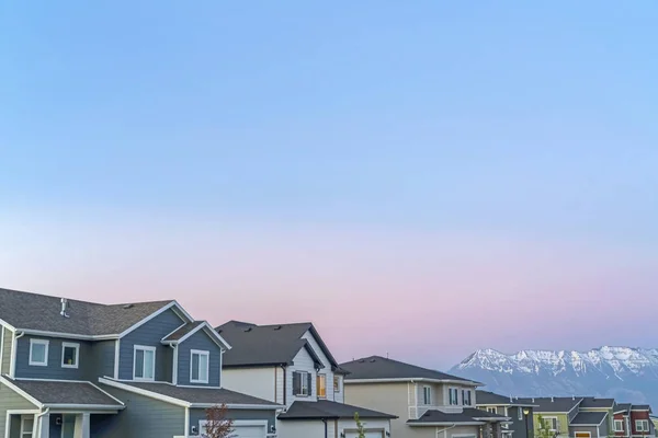 Gün batımında bulutlu mavi gökyüzüne karşı karlı zirvesi olan evler ve dağların dışında. — Stok fotoğraf