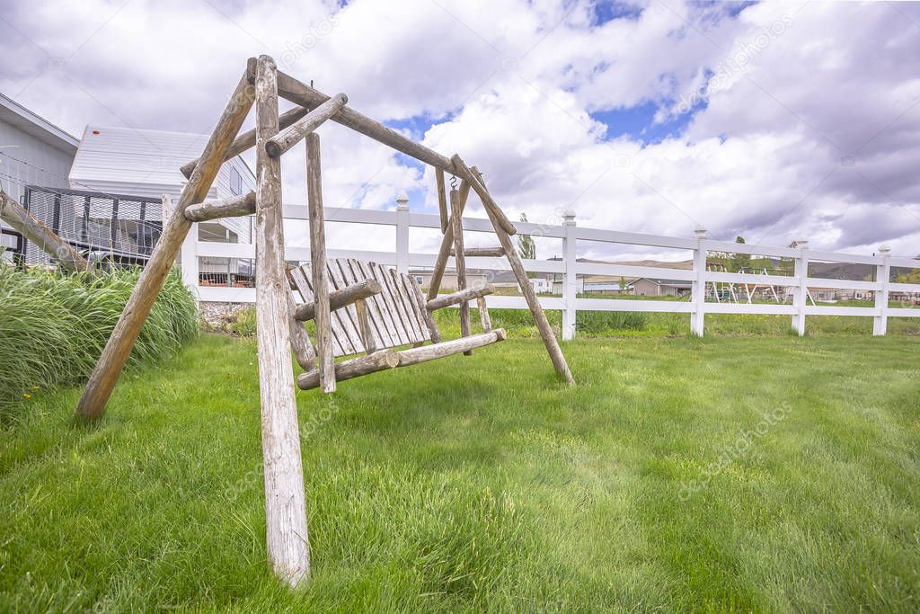 Old wooden garden swing on lush green grasses inside white picket fence