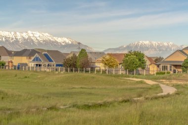 Dar yol ve çimenli arazi, güneşli bir günde evlere ve karlı dağa karşı.