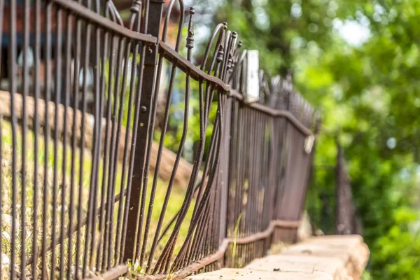 Sunny day view of fence on top of stone wall against blurred trees and sky — 스톡 사진