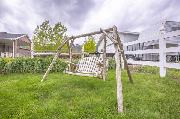 Wooden bench swing at the lush grassy yard of a home with white picket fence