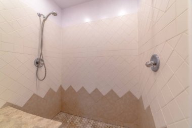 Duvara beyaz ve kahverengi fayanslarla döşenmiş duşlu bir banyo.