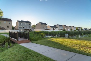 Evlere ve gökyüzüne karşı yemyeşil otlarla dolu bir parkta yol ve köprü.