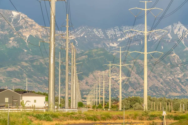Row of high voltage electricity posts with rugged snowy mountain background — 스톡 사진
