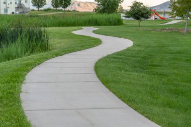 Parkın yemyeşil çimlerinde oyun parkı olan dar asfalt yollar.