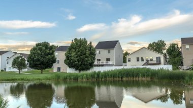 Pano çerçeve evler ve bulutlu gökyüzü parlak bir gölete yansıyan banliyö manzarası