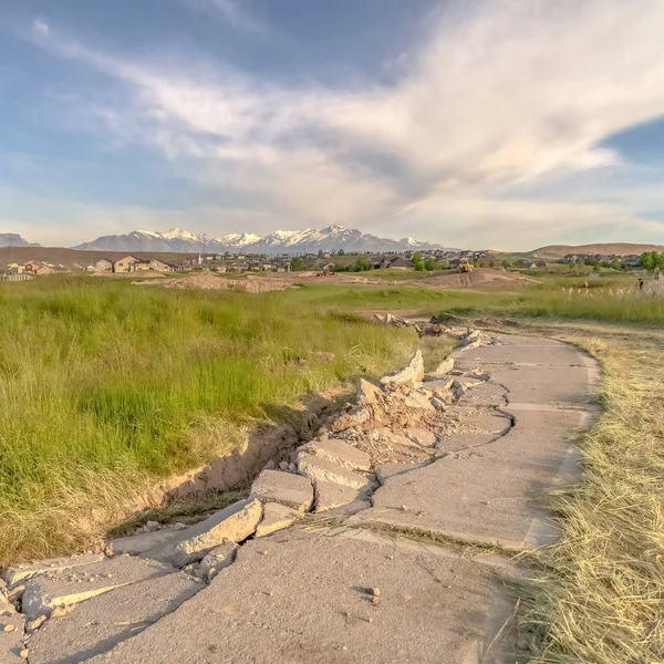 Square Damaged road with view of homes and snow capped mountain against cloudy sky