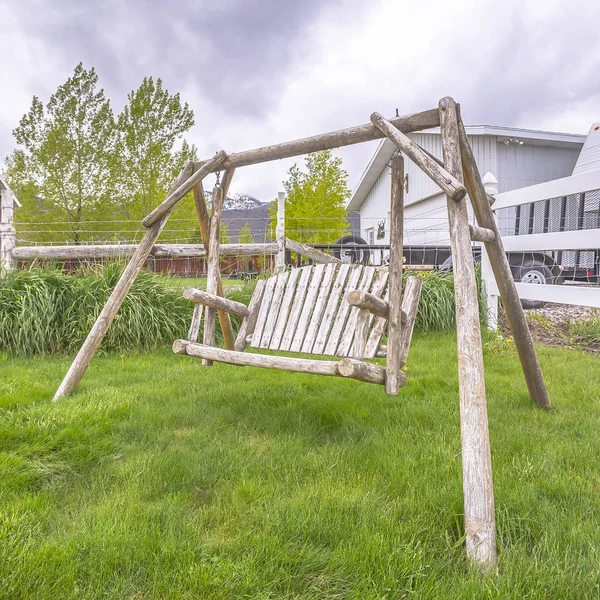 Banco de madeira quadrado balançar no quintal gramado exuberante de uma casa com cerca de piquete branco — Fotografia de Stock