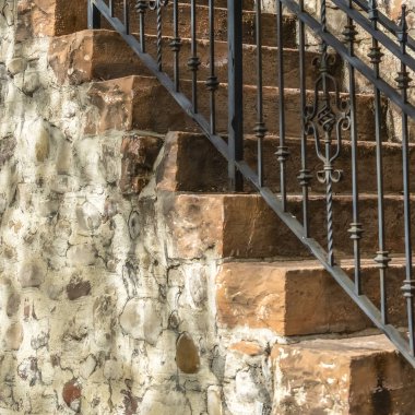 Taş basamaklı kare merdiven ve çite dayanan siyah metal parmaklık.