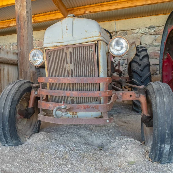 Front carré d'un tracteur ancien et ancien contre un mur de pierre et le toit d'une grange agricole — Photo