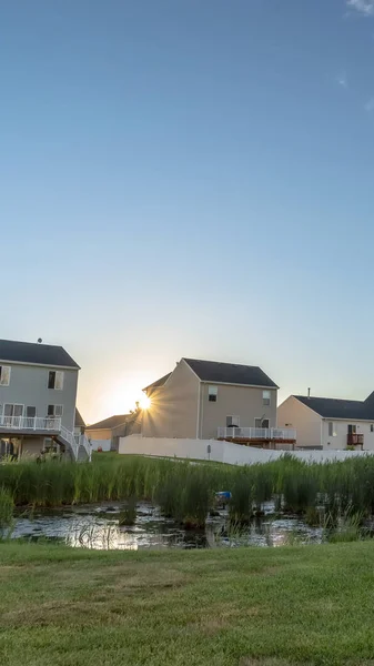 Vistas verticales al atardecer en el suburbio con estanque y casas contra el sol brillante y el cielo azul — Foto de Stock