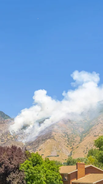 Cadre vertical Ciel bleu clair sur des pentes montagneuses avec des bouffées de fumée provenant d'un feu de forêt sauvage — Photo