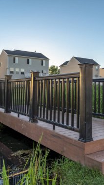 Arka planda evler ve gökyüzü manzaralı gölet ve köprü ile dikey Grassy Parkı