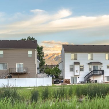 Kare çerçeve Gölet yeşil çimlerle çevrili evler ve dağlar bulutlu mavi gökyüzüne karşı