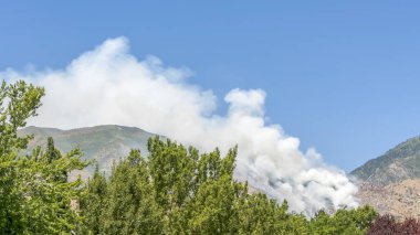 Pano çerçeve Bir dağın yamaçlarında duman Mavi gökyüzüne karşı ateşten güneşli bir günde