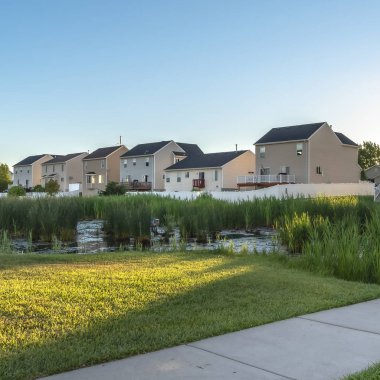 Kare çerçeve Pathway ve gölet üzerinde köprü üzerinde bir parkta yemyeşil çimenler evler ve gökyüzü karşı