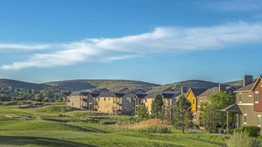 Pano Evleri, dağ ve mavi gökyüzünün manzaralı arka planına sahip bir golf sahası etrafında.
