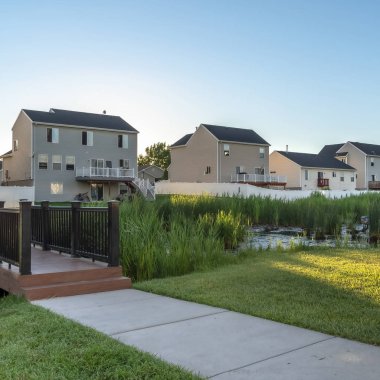 Evlere ve gökyüzüne karşı yemyeşil otlarla dolu bir parkta, gölün üzerinde köprü ve yol.