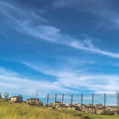 Evleri ve manzaralı arka planda karlı dağları olan kare golf sahası çitleri.