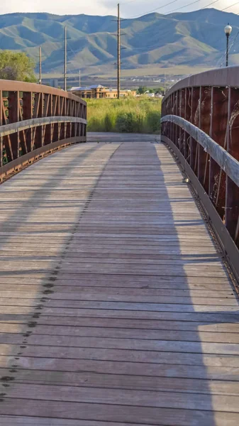 Cornice verticale Ponte in legno illuminato dal sole e ringhiera metallizzata del ponte sul lago con vista sulle montagne — Foto Stock
