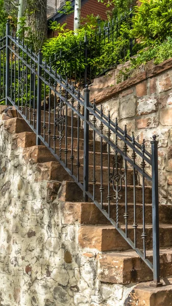 Vertical Outdoor staircase with stone steps and black metal railing against a fence — 스톡 사진