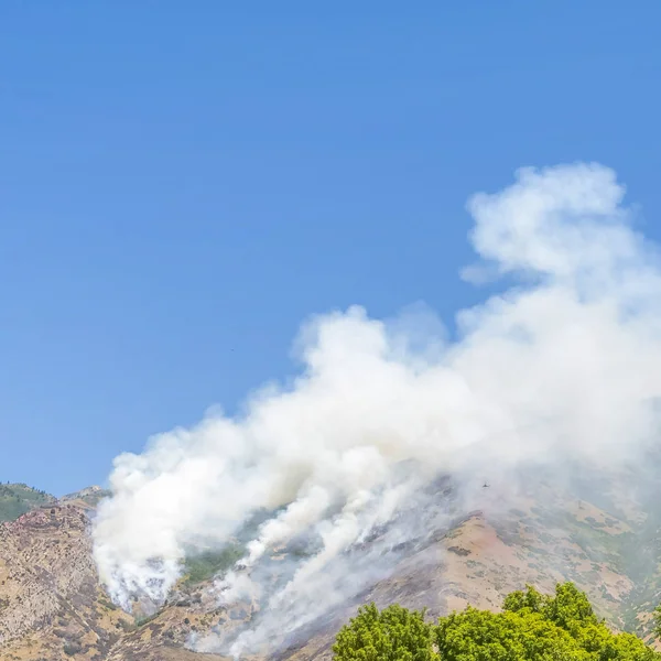 Vue sur la journée ensoleillée carrée avec de la fumée sur le sommet de la montagne depuis un feu de forêt — Photo