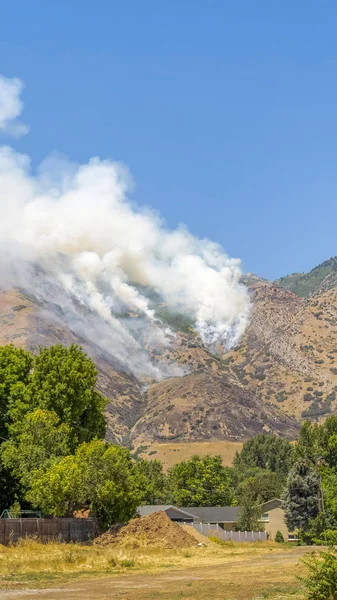 Cadre vertical Feu de forêt sauvage dans la montagne émettant une épaisse fumée blanche contre le ciel bleu — Photo