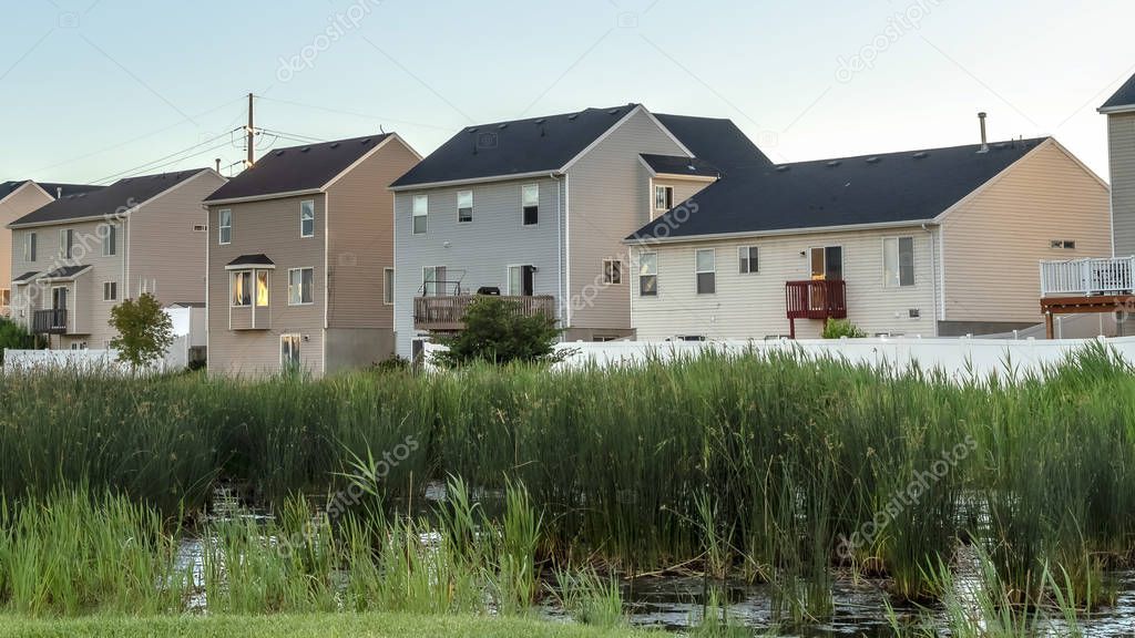 Pano frame Green grasses and pond at a scenic park with houses and blue sky background