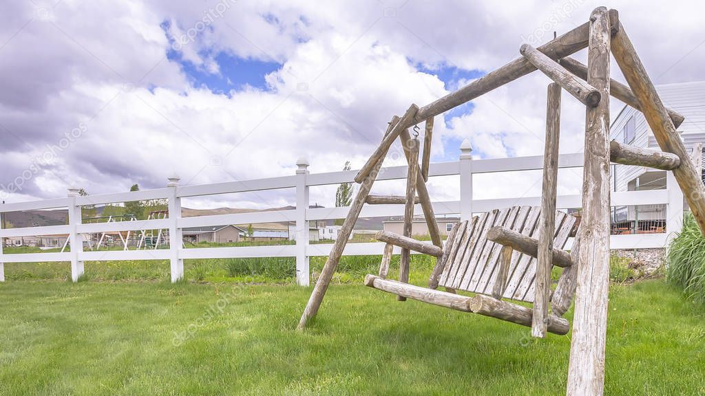 Pano Old wooden garden swing on lush green grasses inside white picket fence