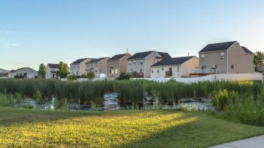 Pano frame Pathway and bridge over pond at a park with lush grasses against houses and sky