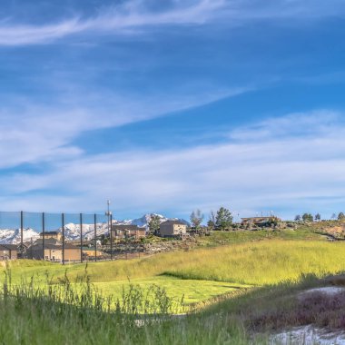 Güneşli bir günde evlerin ve karlı dağların olduğu kare golf sahası manzarası