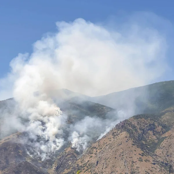 Paysage de montagne carré avec fumée de feu de forêt sauvage contre ciel bleu clair — Photo