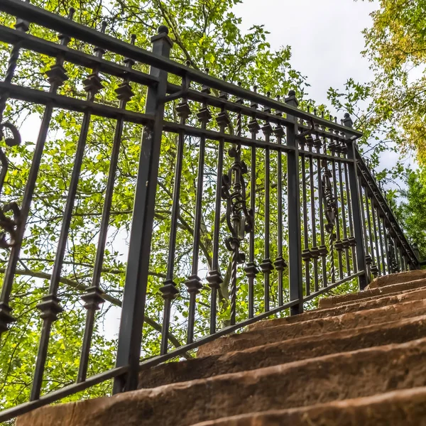 Square frame Close up of staircase with stone treads and metal railing against leaves and sky — 스톡 사진