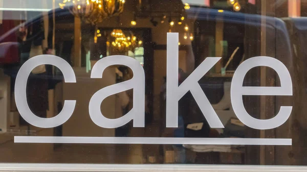 Cadre Pano Gros plan d'un panneau de gâteau blanc sur la fenêtre en verre brillant d'un bâtiment de magasin — Photo