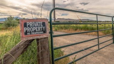 Panorama Security gate and fence with No Trespassing sign against mountain and cloudy sky