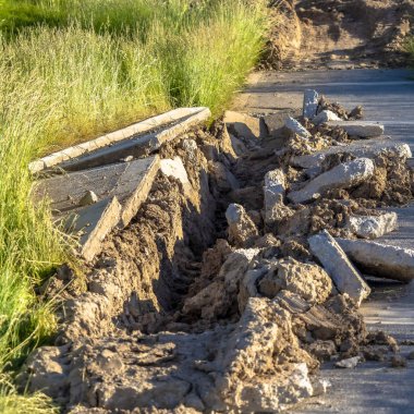 Güneşli bir günde yemyeşil çimlerle kaplı hasarlı beton yolu kapatın.