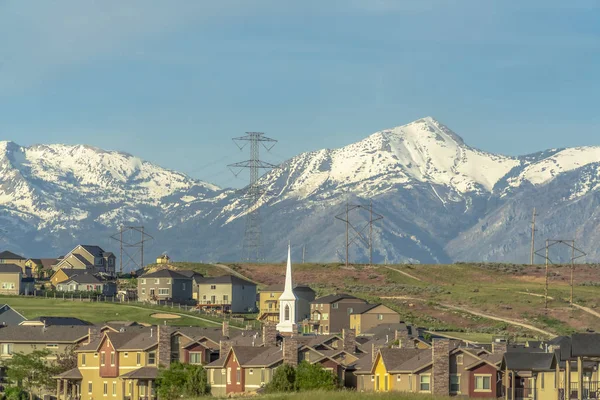 Κτίρια εκκλησία και τα σπίτια γύρω από γήπεδο γκολφ κατά χιονισμένο βουνό και ουρανό — Φωτογραφία Αρχείου