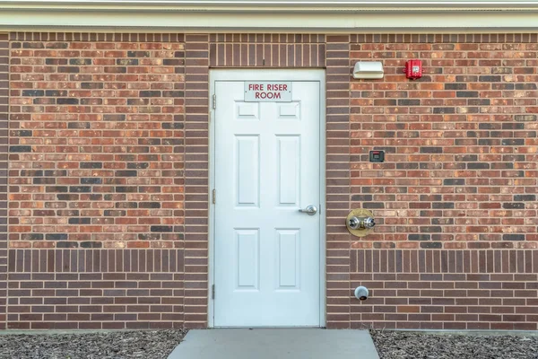 Fire Riser Room sign on the white wood door of a building with red brick wall