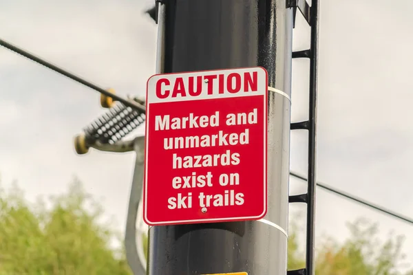 Caution and hazard sign on ski trails and chairlift against blurry trees and sky