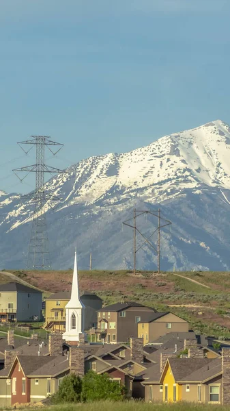 Marco vertical Edificios iglesia y casas alrededor del campo de golf contra montañas nevadas y el cielo — Foto de Stock