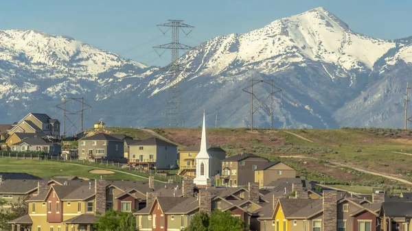 Panorama Buildings church and homes around golf course against snowy mountain and sky