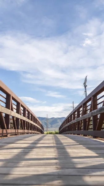 Vertical Focus on bridge with brown lattice metal railing and sunlit wooden deck