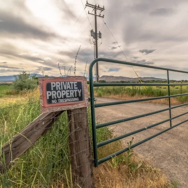 Square Security gate and fence with No Trespassing sign against mountain and cloudy sky — Stock Photo, Image