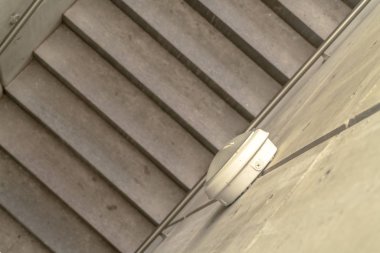 Merdivenlerin üstünden metal parmaklıklar ve yan duvarlarda yuvarlak ışıklar görünüyor.