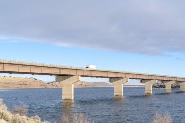 Köprüde bir kamyon akroo mavi göl tepelere ve bulutlu gökyüzüne bakıyor