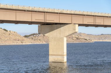 Mavi göl suyu üzerindeki köprü ve iskele temeli dağ ve mavi gökyüzüne karşı